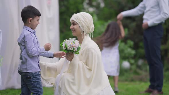 Loving Middle Eastern Little Son Giving Wedding Bouquet to Beautiful Mother Getting Married Outdoors