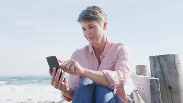 Caucasian woman enjoying free time by sea on sunny day using smartphone