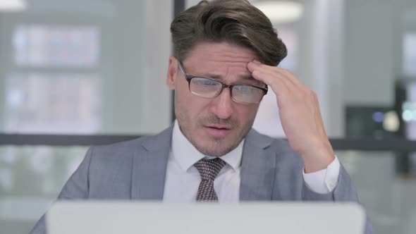 Close Up of Middle Aged Businessman with Laptop having Headache