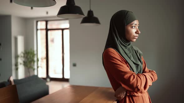 Concentrated Muslim woman wearing hijab standing in kitchen