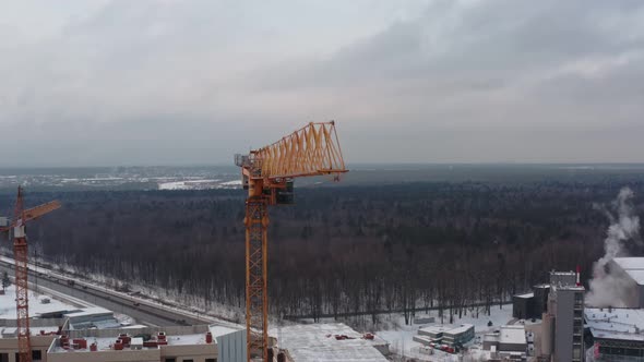 Yellow Tower Crane at Work at the Height of a Large Construction Site Against the Background of