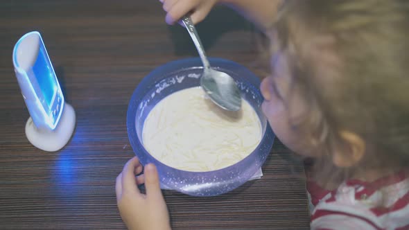 Little Girl Eats Milk Pasta Looking at Baby Monitor at Table