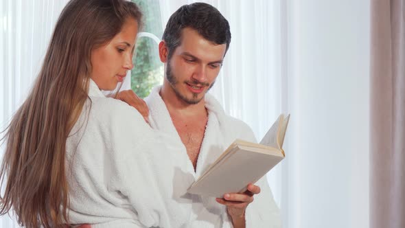 Happy Couple Wearing Bathrobes Reading a Book Together