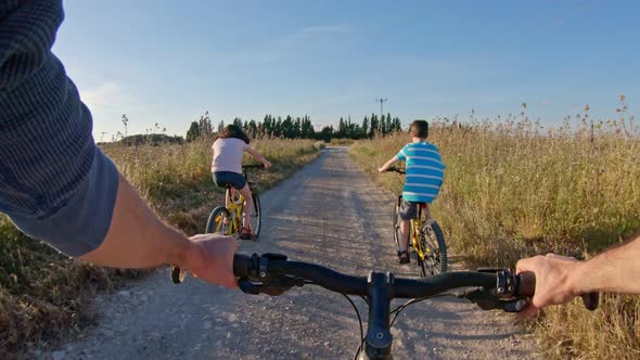 POV of two kids enjoying a bicycle ride on the countryside with their father