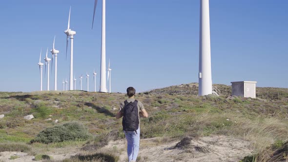 Young man walking through paths towards wind turbines.