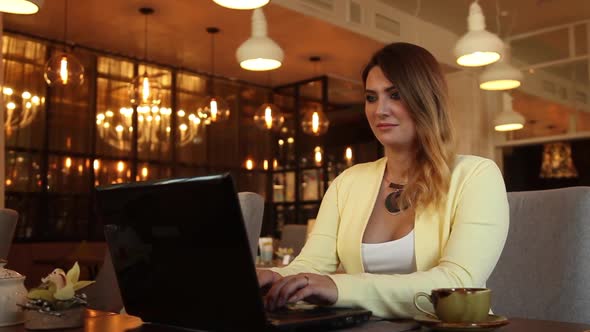 Business Woman with Long Hair in Business Clothes Typing on a Mobile Computer Sitting at a Table