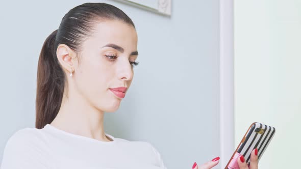 Attractive Young Woman with Bright Manicure Uses Smartphone and Smiles