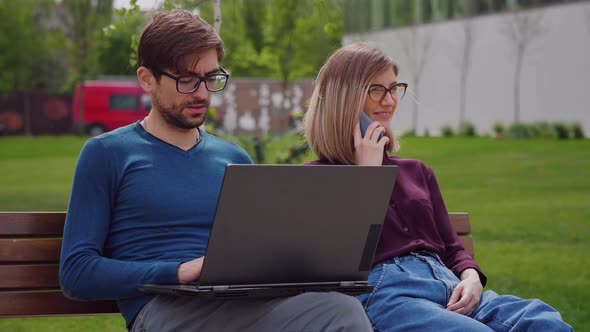 Two professional coworkers sitting on bench spring background.