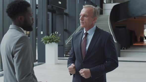 Polite Caucasian Businessman Talking with Black Visitor in Hallway