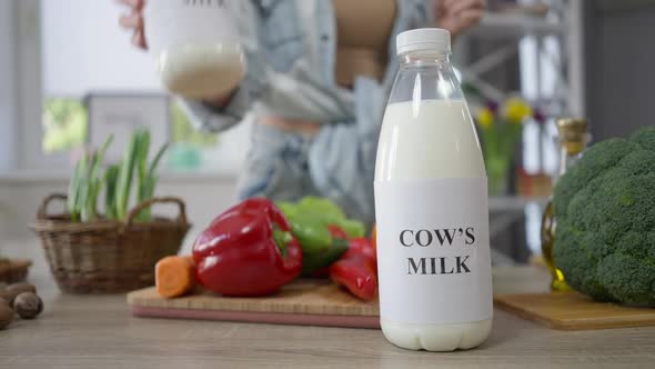 Soy Milk and Cow's Milk on Table in Kitchen with Female Hand Choosing Healthful Nondairy Drink
