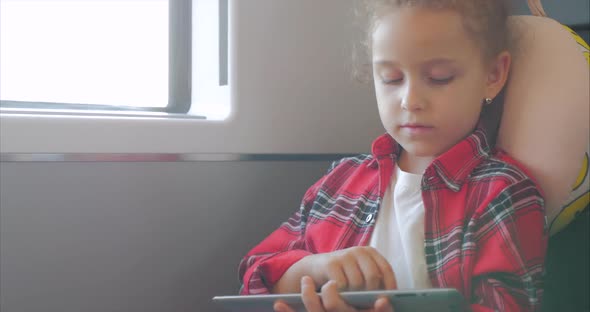 Cute Little Girl Entertaining With Tablet. Child Spending Leisure Time, Rides an Electric Train