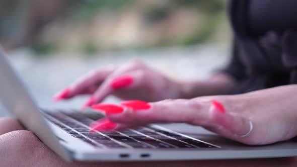 Successful Business Woman with Bright Red Manicure Typing on Laptop Keyboard Outdoors on Beach with