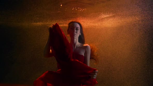 a Brunette with Long Hair and a Red Dress Hovers in a Stream of Bubbles Under the Water. She Looks