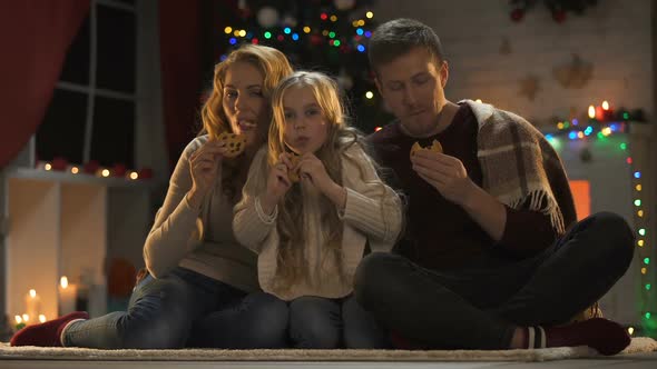 Family Eating Sweet Cookies on Floor, Christmas Tree and Lights Sparkling, Eve