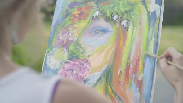 Unrecognizable Woman Painting Summer Woman's Portrait Outdoors, Shooting Over Shoulder of Confident