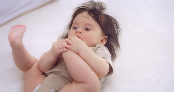 Baby Girl Lies on a Bed in the Nursery Plays and Chewing Foot