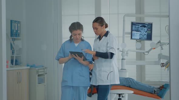 Professional Dentist Talking to Nurse and Looking at Digital Tablet