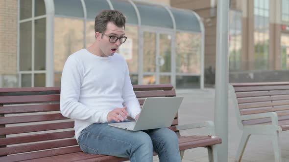 Young Man Reacting to Loss on Laptop While Sitting Outdoor on Bench