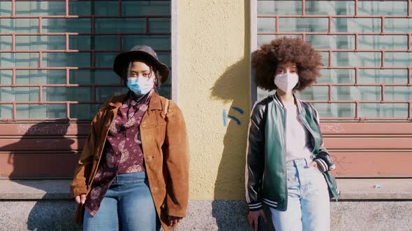 Girlfriends with protective face masks leaning cool against building