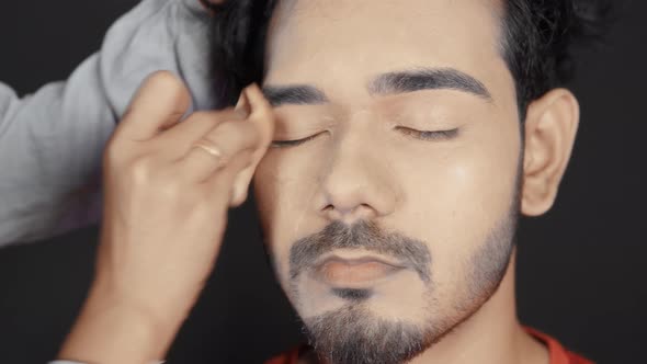 Make up artist putting a face powder on man's face with cosmetics sponge