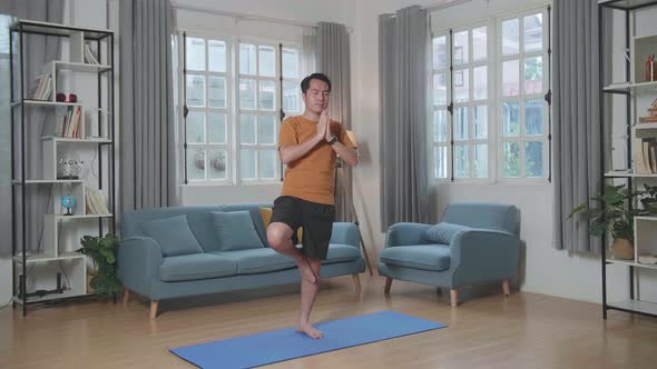 Asian Man Doing Yoga In Tree Pose On Mat  At Home