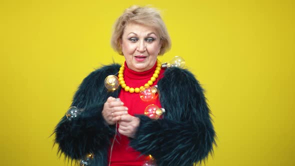 Positive Senior Caucasian Woman in Fur Coat Turning on Garland and Smiling at Camera