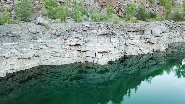 Rocky cliff reflects in green water and tourist in summer clothes looking into it.