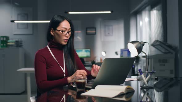Young Asian Woman Working on Laptop in Modern Office