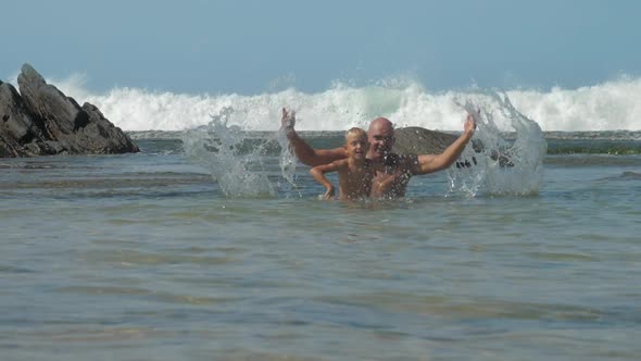 Daddy and Son Splash Playing in Sea Against Huge Waves