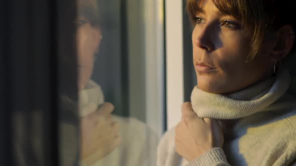 Dreamy woman standing near window and looking away