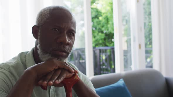 African american man holding walking stick while sitting on the couch at home