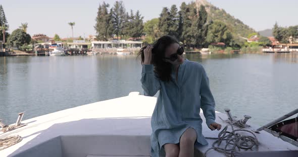Girl tourist is sitting on the boat nose. Mountains in the background.