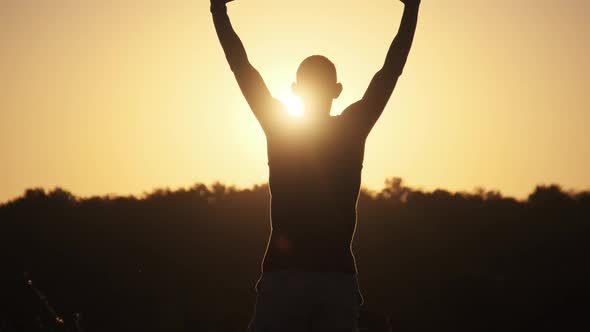 Silhouette of Young Man Against Sunset Raising Hands Sides and Up. Slow Motion