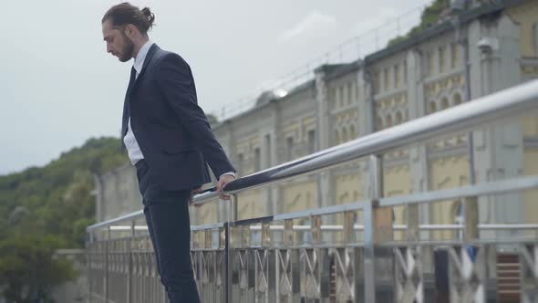 Side View Wide Shot of Desperate Caucasian Businessman in Suit Standing at Bridge Edge Attempting To