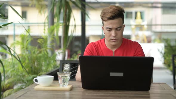 Happy Young Asian Man Using Laptop at the Coffee Shop Outdoors