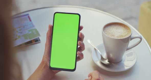 Crop View of Female Person Holding Smartphone and Swipping Greencreen While Sitting at Table with