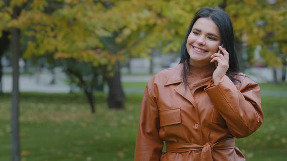 Young Smiling Woman Outdoors in Autumn Park Talking on Mobile Phone Hispanic Girl Enjoys Pleasant