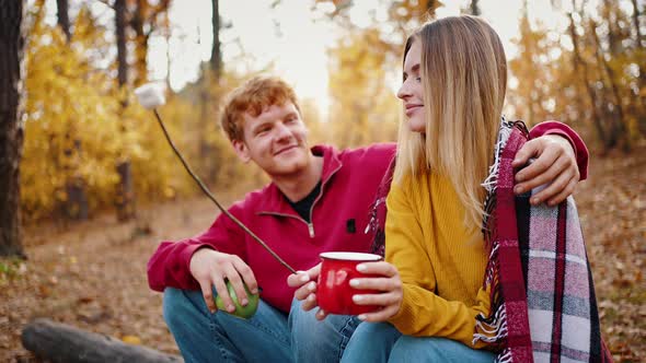 Young Male Smiling Hugging Girlfriend Holding Cup of Tea and Marshmallow on Dry Branch