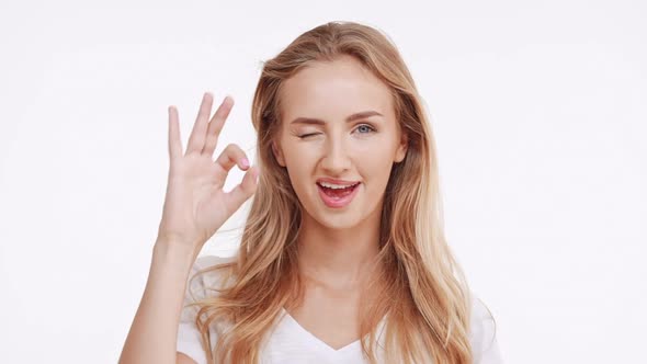 Young Beautiful Caucasian Blonde Girl Showing Ok and Smiling on White Background in Slowmotion