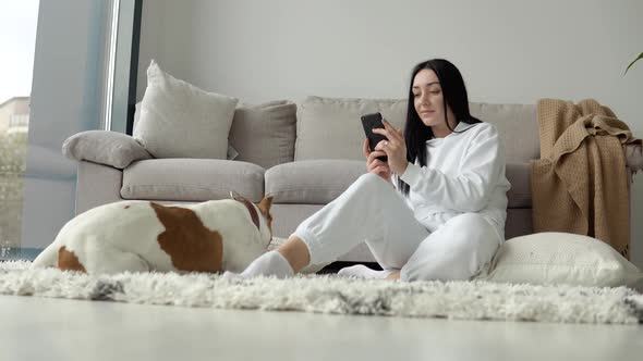 Young Woman Relaxing with Her Dog and Use Phone in a Beautiful Modern Apartment