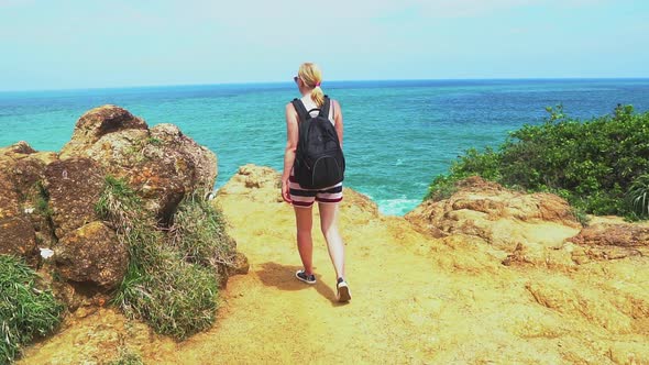 Back view of woman with backpack hiking in tropical island mountains during