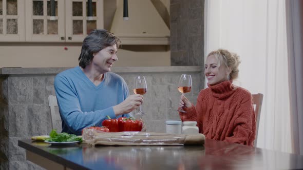 Handsome man and blonde woman with a glass of wine have dinner in the kitchen at home.