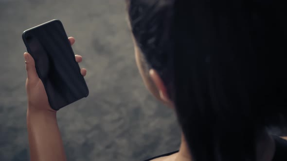 Back View of Fitness Woman Using Smart Phone at Home. Woman Preparing for Workout Using Smart Phone