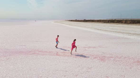 Aerial Drone Footage of Happy Young Couple in Pink Wear Having Fun and Joyfully Running on White