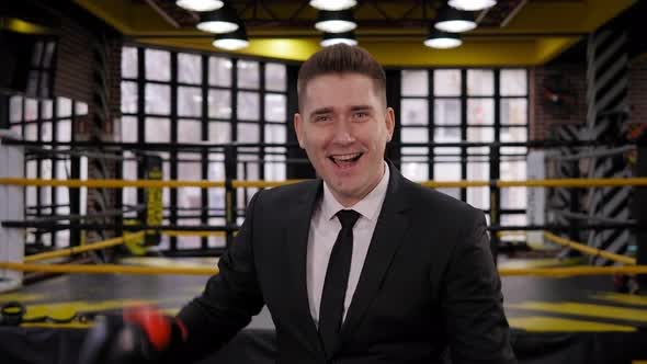 Portrait of a Businessman in a Black Suit and Boxing Gloves on a Boxing Ring