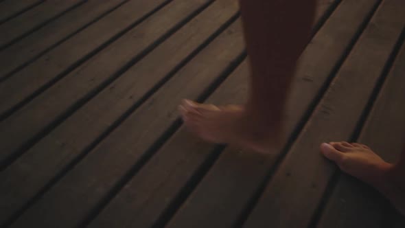 Cropped Picture of Female Tanned Legs Walking Along Wooden Jetty Barefoot During Amazing Sunset with