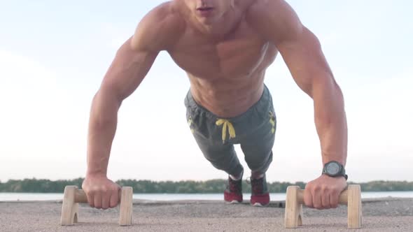 Muscular athletic young man doing pusр ups on the parallettes bar. Sport and health care concept