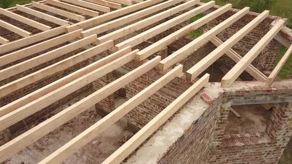 Aerial view of a brick house with wooden ceiling frame under construction.