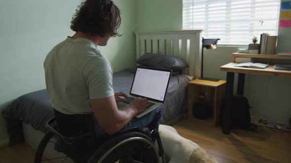 Caucasian disabled man sitting in wheelchair using laptop in bedroom