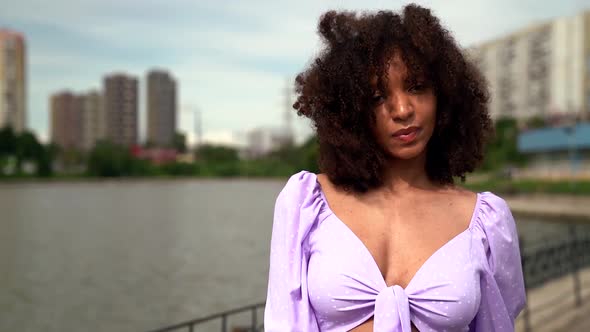 Portrait of a Young African Woman in a Lilac Top with Ties and Puffy Sleeves. She Walks Along the